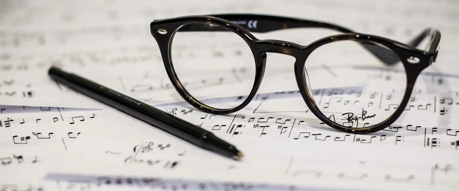 Une photo en format paysage d'une paie de lunette et d'un stylo placés sur des partitions de musique